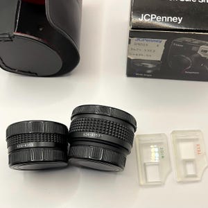 May include: Black camera lenses with the number 624-4353 printed on them. The lenses are next to two clear plastic lens attachments labeled "WIDE" and "TELE". A black camera case and a JCPenney box are also in the image.
