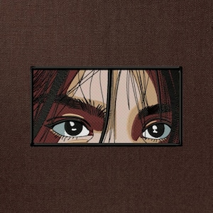 Könnte beinhalten: Gestickter Aufnäher mit einer Anime-Illustration von Augen. Die Augen haben hellblaue Iris, dunkle Pupillen und lange Wimpern. Der Aufnäher ist schwarz umrandet und vor einem braunen Stoffhintergrund platziert.