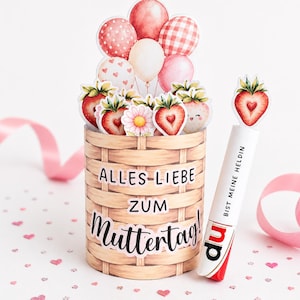 May include: A decorative basket with a woven design, filled with strawberry and flower cutouts, and balloons. The basket has text that reads "Alles Liebe Zum Muttertag!". A pen with the text "Bist Meine Heldln" is next to the basket.