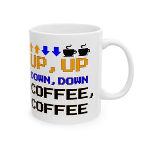 May include: A white ceramic mug featuring pixelated graphics and text. The design includes orange up arrows, blue down arrows, and black coffee cup icons. The text reads: UP, UP DOWN, DOWN COFFEE, COFFEE in a blocky, retro-style font.