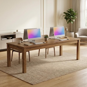 May include: A long rectangular wooden desk with a natural grain finish, featuring two computer monitors with colorful gradient screens, two keyboards, two computer mice, and a small potted plant placed centrally on the tabletop surface.