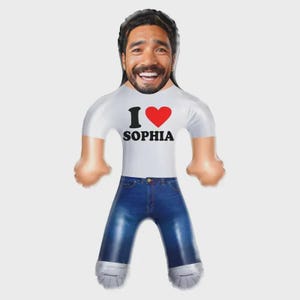 Könnte beinhalten: Aufblasbare Puppe mit lächelndem Gesicht und dunklem Haar, trägt ein weißes T-Shirt mit dem Aufdruck "I ♥ SOPHIA" und eine blaue Jeans. Die Puppe hat aufgeblasene Arme und Beine sowie silberfarbene Fußbedeckungen.