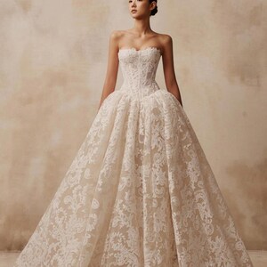 May include: A strapless floor-length ball gown featuring a fitted corset bodice and a voluminous skirt. The dress is crafted from a light beige fabric overlaid with intricate white floral lace patterns that extend from the bodice to the hem.