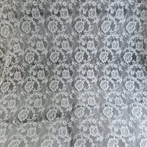 Peut inclure: Un tissu en dentelle blanche pr&eacute;sentant un motif floral complexe avec des bords festonn&eacute;s. Le textile d&eacute;licat affiche un design botanique r&eacute;p&eacute;titif avec des d&eacute;tails en maille fine sur toute la surface, cr&eacute;ant un aspect semi-transparent.