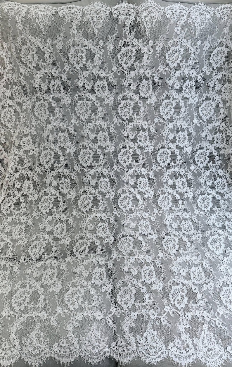 Peut inclure: Un tissu en dentelle blanche pr&eacute;sentant un motif floral complexe avec des bords festonn&eacute;s. Le textile d&eacute;licat affiche un design botanique r&eacute;p&eacute;titif avec des d&eacute;tails en maille fine sur toute la surface, cr&eacute;ant un aspect semi-transparent.