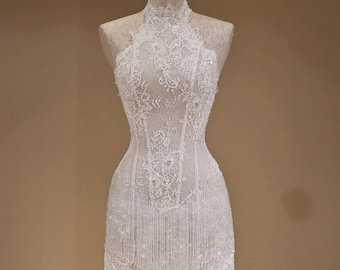 May include: A white sleeveless mini dress featuring a high halter neckline and intricate floral lace overlay. The bodice is structured with visible boning, while the skirt is adorned with long, delicate fringe trim that hangs from the hemline.