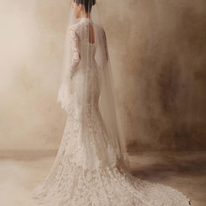 Peut inclure: Une robe de mari&eacute;e en dentelle blanche longue jusqu'au sol avec des manches longues, un col montant et une ouverture en forme de goutte au dos. La robe pr&eacute;sente une superposition de dentelle florale, un corsage ajust&eacute; et une longue tra&icirc;ne.