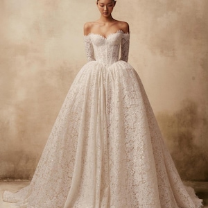 Peut inclure: Une robe longue &agrave; &eacute;paules d&eacute;nud&eacute;es dot&eacute;e d'un corsage ajust&eacute; et d'une jupe volumineuse. L'ensemble du v&ecirc;tement est confectionn&eacute; en dentelle blanche avec des motifs floraux complexes et de subtiles d&eacute;corations &agrave; paillettes sur tout le tissu.