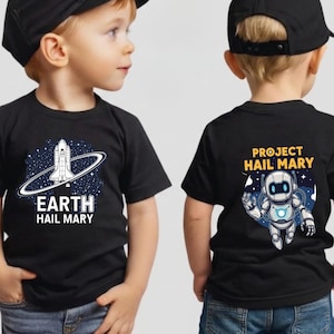 Może przedstawiać: Dwie czarne koszulki z białą grafiką i tekstem. Jedna koszulka przedstawia wz&oacute;r statku kosmicznego ze słowami "EARTH HAIL MARY". Druga koszulka przedstawia wz&oacute;r robota ze słowami "PROJECT HAIL MARY".