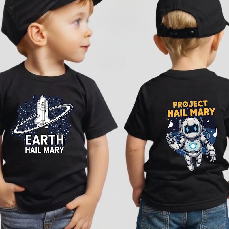 Może przedstawiać: Dwie czarne koszulki z białą grafiką i tekstem. Jedna koszulka przedstawia wz&oacute;r statku kosmicznego ze słowami "EARTH HAIL MARY". Druga koszulka przedstawia wz&oacute;r robota ze słowami "PROJECT HAIL MARY".