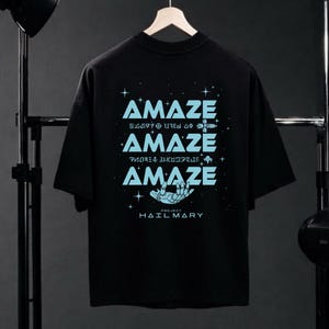 Może przedstawiać: Czarny t-shirt ze słowem "AMAZE" w jasnoniebieskim kolorze, powt&oacute;rzonym trzy razy r&oacute;żnymi czcionkami. Projekt zawiera grafikę dłoni i tekst "PROJECT HAILMARY".
