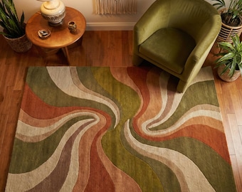 May include: A rectangular area rug with a retro design. The rug features swirling, curved stripes in shades of green, orange, brown, and beige. The rug is placed on a hardwood floor, with a green chair and plants in the background.