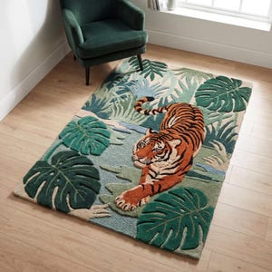 May include: A rectangular rug featuring a tiger in a jungle setting. The rug has a blue, green, and beige color scheme with large green leaves and a tiger with orange and black stripes. The rug is placed on a wooden floor.