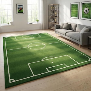 Puede incluir: Una alfombra rectangular verde que simula un campo de fútbol, con marcas blancas para los límites, el círculo central y las áreas de portería. La alfombra está colocada sobre un suelo de madera clara en un salón.