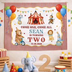 May include: A circus-themed birthday party banner with red and white stripes, balloons, and the text "COME ONE, COME ALL SEAN IS TURNING TWO 12.28.2026". Includes a plush elephant, wooden number 2, and party decorations.