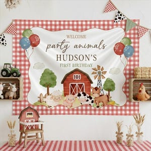 May include: A farm-themed party backdrop with a red and white checkered pattern. The banner reads "Welcome Party Animals Hudson's First Birthday" with illustrations of farm animals, a barn, and a windmill. Balloons and decorative elements complete the festive scene.