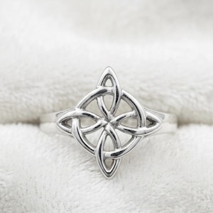 May include: A silver-colored ring featuring a Celtic knot design. The ring's intricate knotwork is centered on the band, with a symmetrical pattern of interwoven lines. The ring is set against a soft, white background.