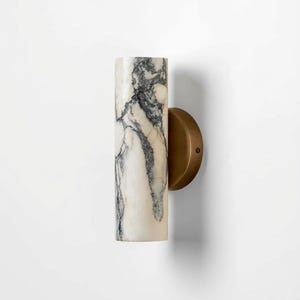 Peut inclure: Applique murale cylindrique avec un motif marbré. L'applique a un fond blanc avec des veines noires et une base circulaire en laiton. Le luminaire est conçu pour être monté au mur et fournit un éclairage ambiant.