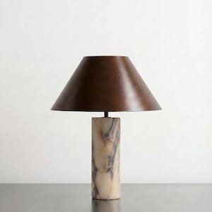 May include: A contemporary table lamp featuring a brown lampshade and a marble base. The cylindrical base has beige, grey, and black veining. The lampshade is a dark brown, cone-shaped design.