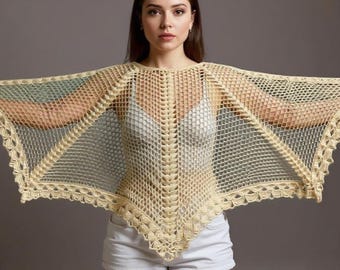 Puede incluir: Un chal de crochet crema de tejido abierto con un borde festoneado. El chal está drapeado sobre los hombros, creando una silueta de ala de murciélago. La prenda está hecha de un material ligero y aireado.