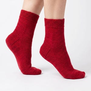 May include: A pair of red socks, knitted from a textured material. The socks are a solid, deep red colour and reach mid-calf. The socks are displayed against a white background.