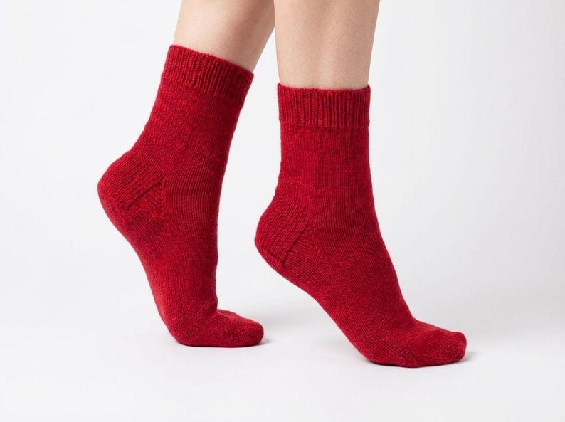 May include: A pair of red socks, knitted from a textured material. The socks are a solid, deep red colour and reach mid-calf. The socks are displayed against a white background.