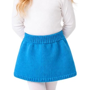May include: A white long-sleeved ribbed shirt paired with a bright blue knitted skirt featuring a wide ribbed waistband and hem. The outfit is completed with opaque white tights and simple white lace-up sneakers, creating a clean look.