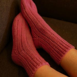 Puede incluir: Un par de calcetines rosas de punto. Los calcetines tienen un diseño acanalado en la parte superior y un diseño estampado en la parte delantera. Los calcetines son de un tono rosa vibrante y parecen hechos a mano.