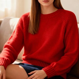 May include: A bright red crew neck sweater with long sleeves. The knitwear features ribbed cuffs and hem. The sweater is made from a soft, textured material. This cosy sweater is suitable for everyday wear.