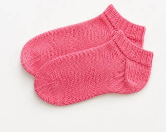 May include: A pair of ankle-length socks in a solid, vibrant pink color. These socks feature a fine-knit texture throughout, with a ribbed cuff at the opening and a reinforced, rounded toe section. The design is simple, low-cut, and uniform.