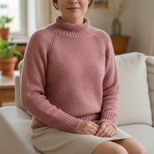 Op de afbeelding: Een stoffig roze coltrui met geribde manchetten en zoom. De trui is gemaakt van een zacht, gebreid materiaal. Het model draagt een lichtbeige rok en zit op een crèmekleurige bank.