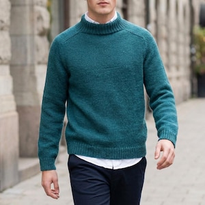 Könnte beinhalten: Ein langärmeliger, blaugrüner Pullover mit geripptem Stehkragen, getragen über einem weißen Hemd mit Kragen und einer dunkelblauen Hose. Der Pullover hat eine Strickstruktur mit Raglanärmeln sowie gerippten Bündchen an Ärmeln und Saum.