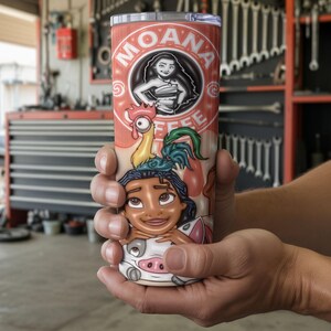 K&ouml;nnte beinhalten: Ein Edelstahlbecher mit einem Cartoon-Design. Der Becher zeigt den Text "MOANA COFFEE" und Illustrationen von Moana und anderen Charakteren auf rotem Hintergrund. Der Becher wird von einer Person in den H&auml;nden gehalten.