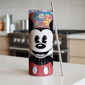 May include: A stainless steel tumbler featuring a smiling Mickey Mouse design. The tumbler has a red and white base with Mickey's iconic shorts. A silver straw is placed next to the tumbler. The top of the tumbler has a colorful illustration.