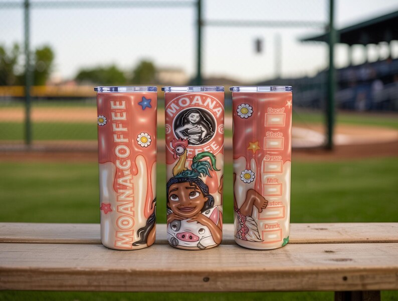 K&ouml;nnte beinhalten: Drei Edelstahlbecher mit korallenfarbenem Hintergrund. Jeder Becher hat ein anderes Design aus dem Film Moana. Einer hat die Worte "Moana Coffee", ein anderer Moanas Bild und der dritte Getr&auml;nkemessungen.