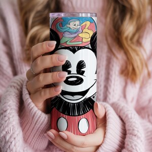 May include: A tall, insulated tumbler featuring a smiling Mickey Mouse design. The tumbler has a red, black, and white color scheme with a cartoon illustration of Mickey Mouse's face and body. The top section has a colorful cartoon illustration.