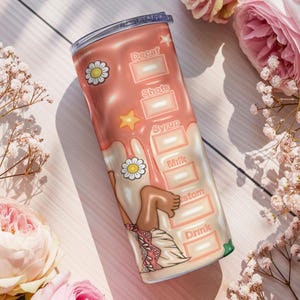 K&ouml;nnte beinhalten: Ein rosa-wei&szlig;er isolierter Becher mit einem Cartoon-Design. Der Becher zeigt die W&ouml;rter "Decaf", "Shots", "Syrup", "Milk", "Custom" und "Drink". Der Becher ist mit G&auml;nsebl&uuml;mchen und einem Stern verziert.