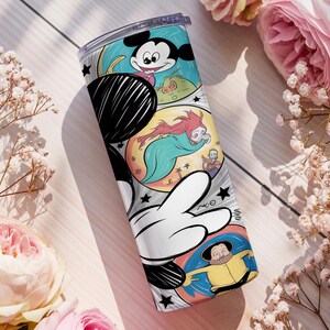 May include: A stainless steel tumbler featuring a colorful comic strip design with Mickey Mouse and other cartoon characters. The tumbler has a black and white Mickey Mouse hand graphic on the side. The background includes pink roses and white flowers.
