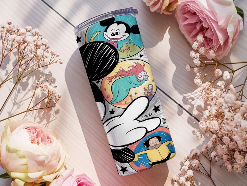 May include: A stainless steel tumbler featuring a colorful comic strip design with Mickey Mouse and other cartoon characters. The tumbler has a black and white Mickey Mouse hand graphic on the side. The background includes pink roses and white flowers.