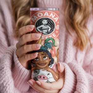 K&ouml;nnte beinhalten: Ein hoher, zylindrischer Becher mit einem Design, das von dem Animationsfilm "Moana" inspiriert wurde. Der Becher hat einen hellbraunen Hintergrund mit den Worten "Moana Coffee" und einer Grafik der Figur Moana. Der Boden des Bechers zeigt die Charaktere Moana und Pua.