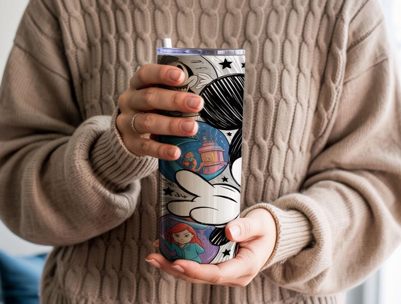 May include: A tall, insulated tumbler with a whimsical cartoon design. The tumbler features a white and black Mickey Mouse hand, with colorful illustrations of characters and scenes. The design includes a blue background with a lantern and a red-haired character.