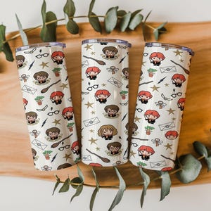 May include: Three cylindrical tumblers with a white background featuring a repeating pattern of cartoon characters, broomsticks, envelopes, glasses, lightning bolts, and gold stars. Each tumbler has a clear lid and a smooth, straight-sided design.