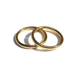 May include: Two polished gold-tone metal rings with a smooth, rounded surface. The rings are circular in shape and feature a high-shine reflective finish that catches the light, creating bright highlights along the curved edges of the bands.