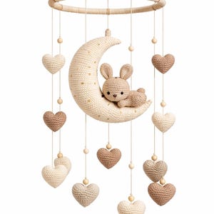 May include: A crochet baby mobile featuring a crescent moon with a sleeping bunny and hanging hearts. The mobile is suspended from a circular ring. The hearts and bunny are in shades of cream and brown, with wooden beads. A charming nursery decoration.
