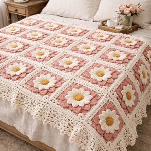 May include: A handmade crochet blanket with a daisy design. The blanket has a pink square base with white daisy flowers and a yellow centre. The edges are finished with a white, scalloped lace trim. The blanket is on a bed with white linens.