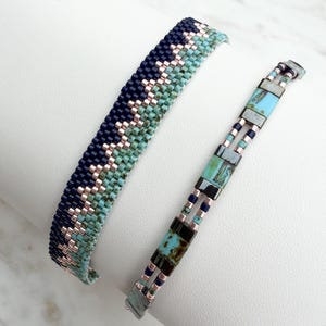 Puede incluir: Dos pulseras de cuentas. Una es ancha, azul marino, turquesa y color cobre. La otra es estrecha, con cuentas rectangulares turquesas y negras, y detalles color cobre. Ambas están sobre una superficie blanca.