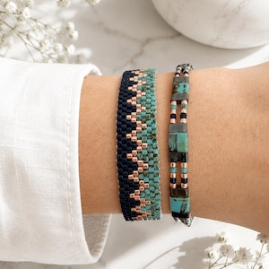 Könnte beinhalten: Zwei Armbänder mit gewebtem Design. Das breitere Armband zeigt ein Zickzackmuster aus marineblauen, kupferfarbenen und türkisfarbenen Perlen. Das schmalere Armband besteht aus abwechselnden türkisfarbenen rechteckigen Perlen sowie marineblauen und kupferfarbenen Elementen.