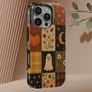 Könnte beinhalten: Eine Smartphone-Hülle mit einem Patchwork-Design, das herbstliche Motive wie einen Kürbis, ein Gespenst, eine Mondsichel, Sterne, Herbstblätter und Blumenmuster in den Farben Orange, Gelb, Braun, Schwarz und Creme zeigt.