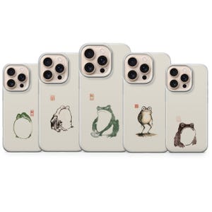 May include: Five phone cases with frog illustrations in various poses and colors. The cases are off-white with a clear camera lens protector. Each case features a different frog design, including green, brown, and black ink drawings.