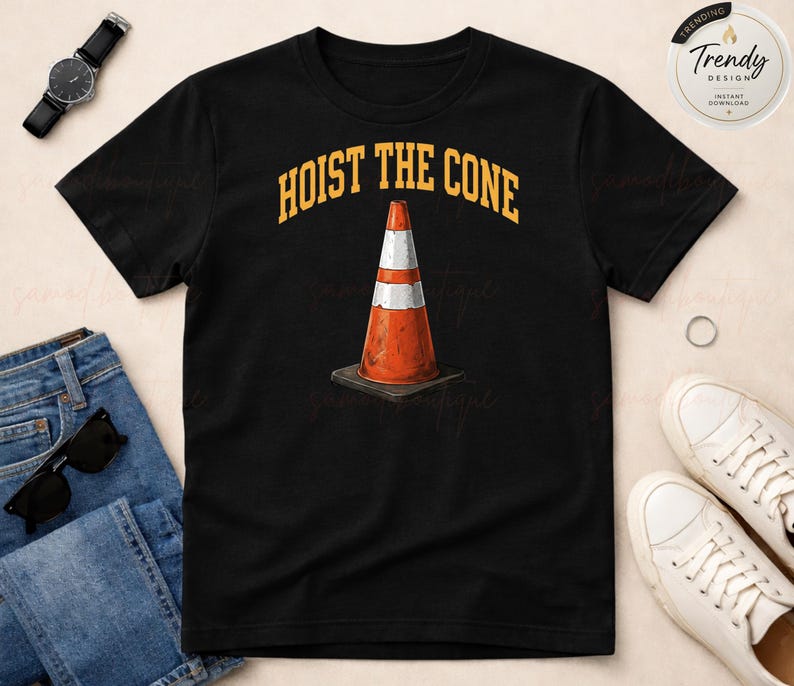 May include: Black t-shirt with the text "HOIST THE CONE" in yellow arched lettering above a graphic of an orange and white traffic cone. The cone is on a black square base. The shirt is displayed with jeans, sunglasses, and white sneakers.